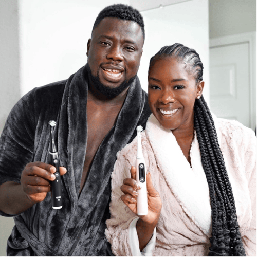 Smiling man and woman in bathrobes displaying electric toothbrushes